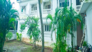 A two-story building with a balcony, surrounded by palm trees and a garden area. - Lillywoods NV beach Resort (Calangute)