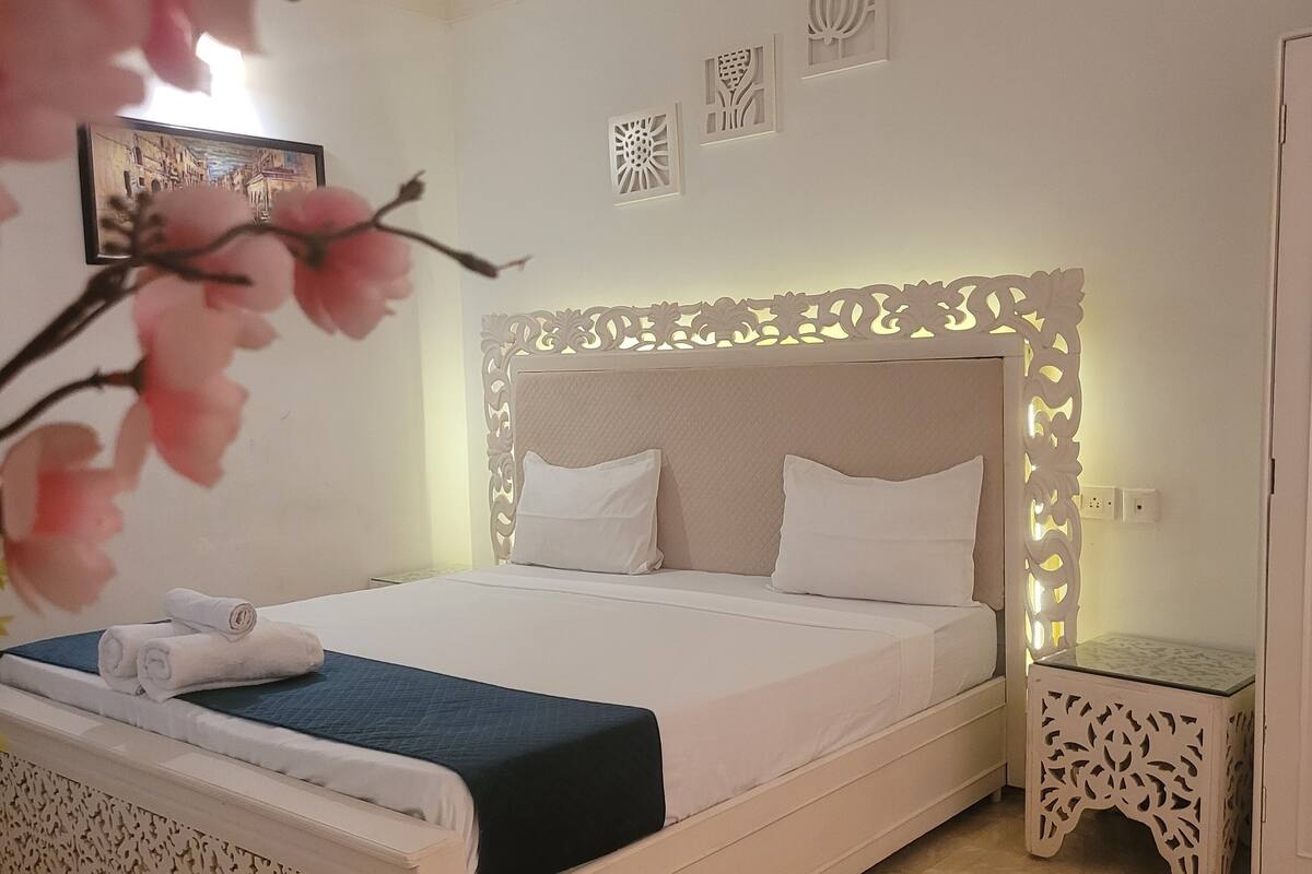 A neatly arranged bedroom with a large bed, a bedside table, and a decorative wall piece.