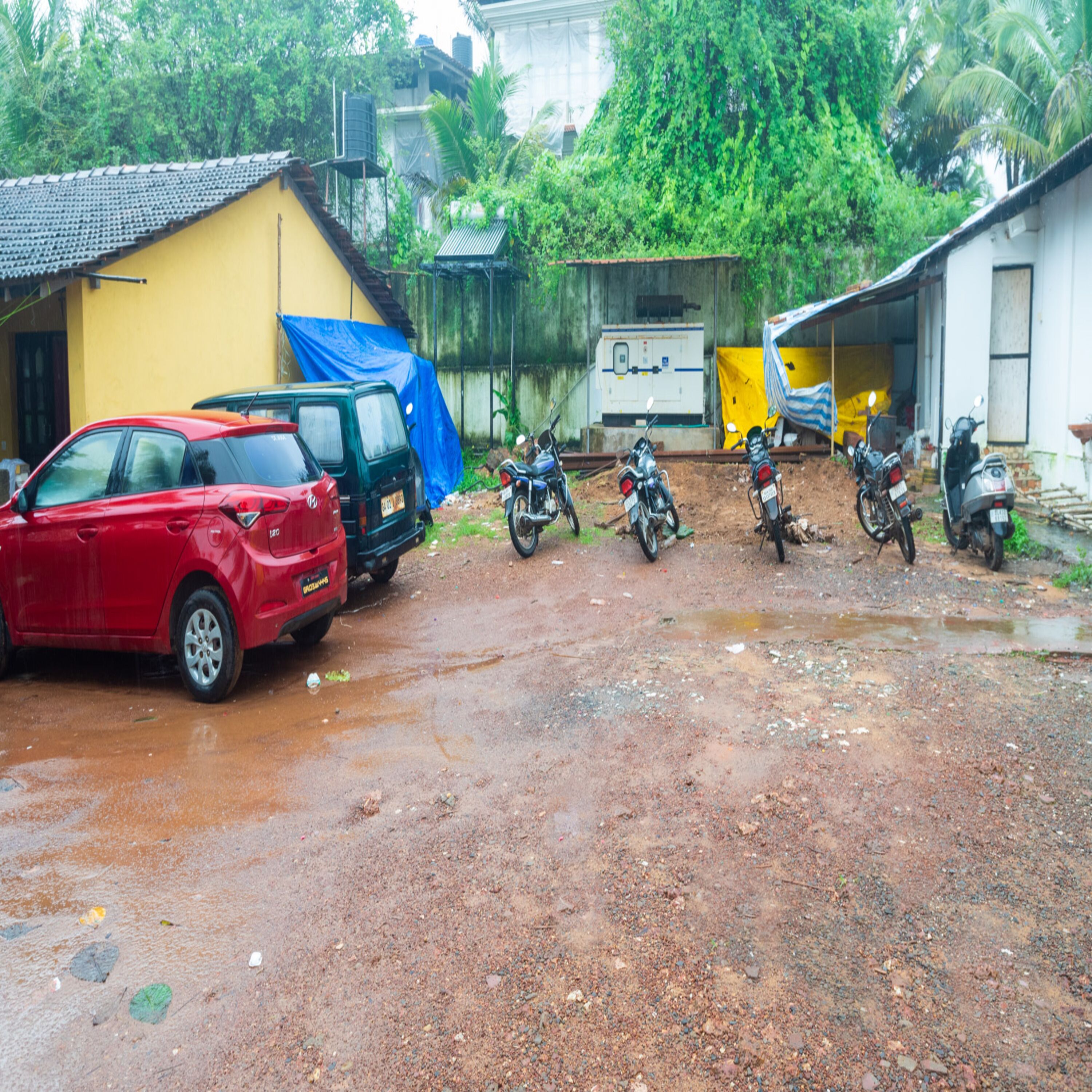A parking area with several motorcycles and a red car parked on a wet surface.