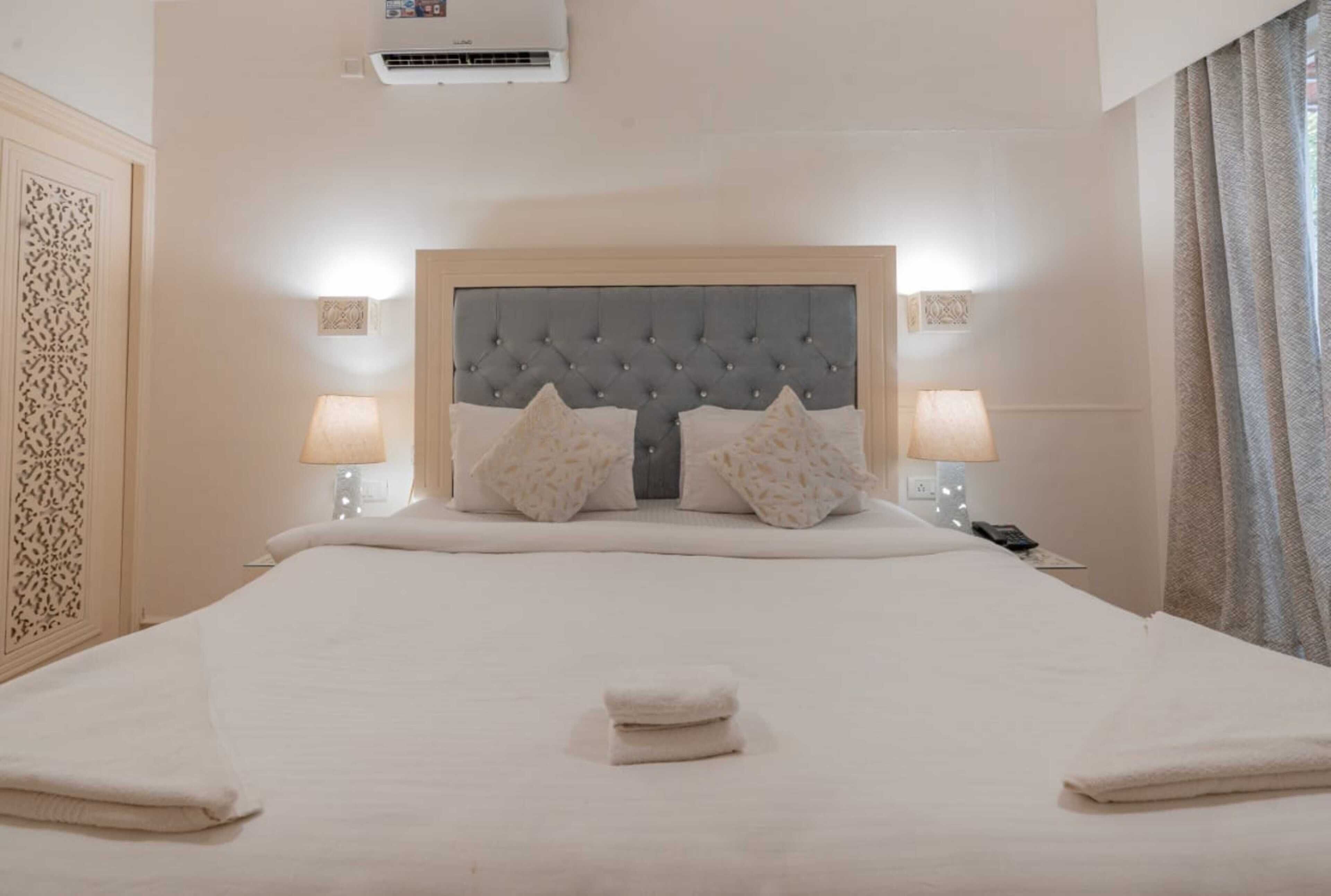Una habitación de hotel con una cama grande, dos lámparas de noche, un cabecero decorativo y una mesita con un teléfono.