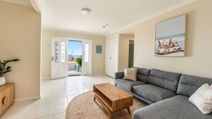 A modern living room with a grey sofa, a wooden coffee table, and a large window offering a view of the beach. - Como - Absolute Beachfront with Uninterrupted Convent Beach Views - Holiday Yamba (Yamba)