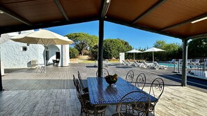 An outdoor covered patio with a dining table, chairs, umbrellas, and a pool area with lounge chairs.