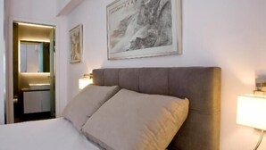 A hotel room with a large bed, a bedside lamp, a framed artwork above the bed, and a bathroom visible through an open door. - SynAthens Apartments & Studios (Athens)