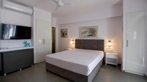 A bedroom with a bed, a TV, a ceiling fan, and artwork on the walls. - SynAthens Apartments & Studios (Athens)