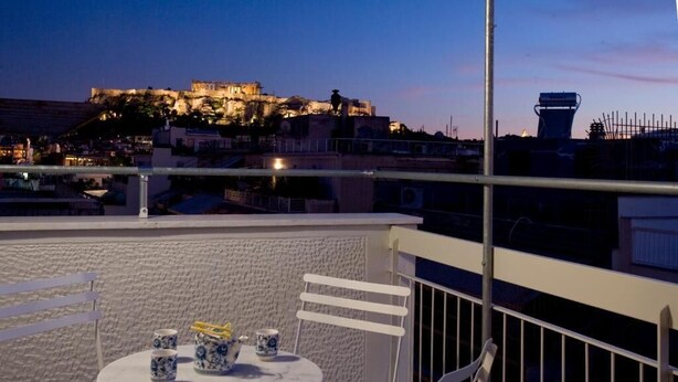 A balcony with a table and chairs, overlooking a historic building with a view of the cityscape. - SynAthens Apartments & Studios (Athens)