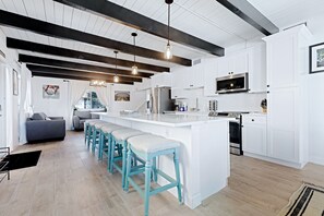 Una cocina moderna con armarios blancos, una isla central con taburetes y un comedor con sofá y sillas.