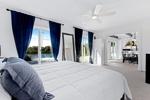 Ein modernes Hotelzimmer mit einem großen Bett, einem Deckenventilator und Blick auf einen Pool sowie eine Außenlounge.