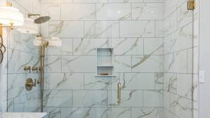 A modern bathroom with a glass-enclosed shower, marble tiles, and a vanity with blue cabinets and gold handles. - Luxury French Quarter 1bd Suite w. Parking (Charleston)