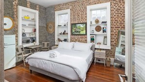 A bedroom with a brick wall, a bed, a desk, and shelves with various items. - Luxury French Quarter 1bd Suite w. Parking (Charleston)