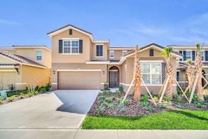 A two-story house with a garage, a front yard with palm trees, and a clear sky.