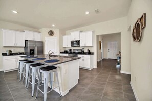 Una cocina moderna con armarios blancos, una isla central con taburetes altos, electrodomésticos de acero inoxidable y un microondas.
