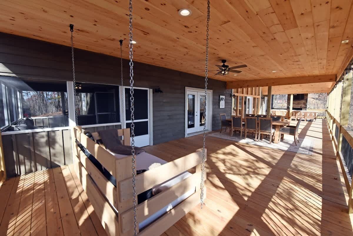 Una terraza de madera con un columpio, un comedor y vistas al exterior.