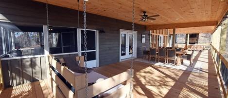 Una terraza de madera con un columpio, un comedor y vistas al exterior.