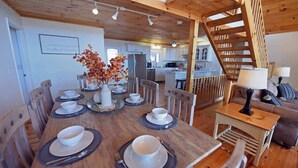 Un comedor con una mesa de madera dispuesta para cuatro personas, una escalera y una cocina al fondo.