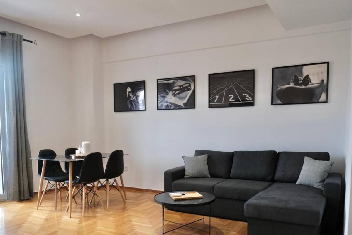 A modern living room with a black sofa, a dining table with chairs, and four framed artworks on the wall.