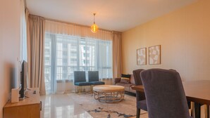 A modern living room with a flat-screen TV, a wooden desk, a round coffee table, and a dining table with chairs. - Bella Vista - 29 Boulevard Downtown - 2BR - Partial Fountain View (Dubai)