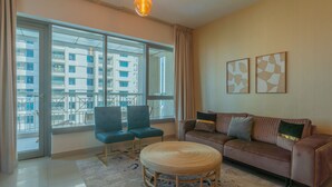 A modern living room with a large window, a sofa, two chairs, a round coffee table, and abstract wall art. - Bella Vista - 29 Boulevard Downtown - 2BR - Partial Fountain View (Dubai)