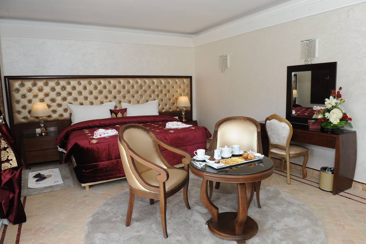 Ein Hotelzimmer mit einem großen Bett, zwei Stühlen, einem kleinen Tisch mit Frühstück, einem Schreibtisch und einem Spiegel.