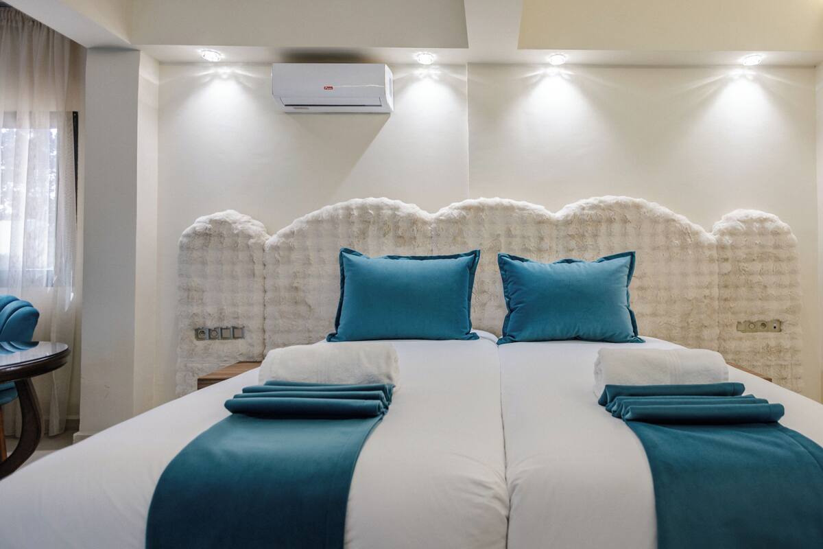 Ein Hotelzimmer mit einem großen Bett, zwei Kissen, einem weißen Kopfteil und einer Klimaanlage.