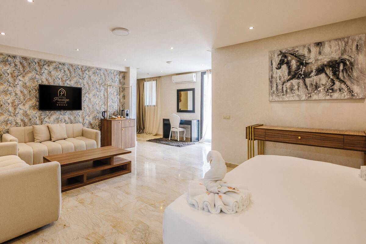 Ein Hotelzimmer mit Marmorboden, einer Couch, einem Bett, einem Fernseher, einem Schreibtisch und einem Gemälde.