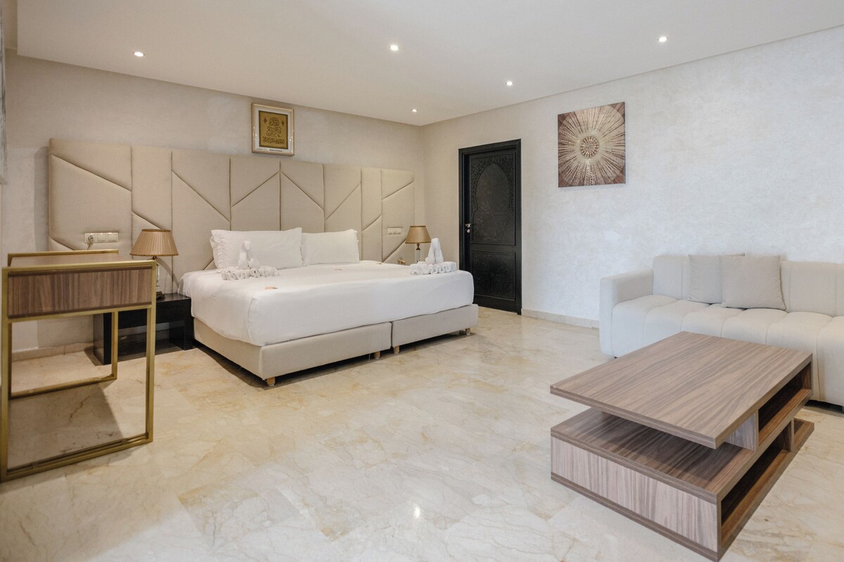 A modern hotel room with a bed, a sofa, a coffee table, and artwork on the walls.
