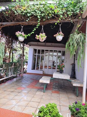 A covered patio with hanging flower baskets, a bench, and potted plants. - Lux suites Utawala Family House (Nairobi)