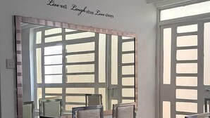 Un comedor con una mesa de mármol, sillas acolchadas, un espejo grande y una cita motivadora en la pared.