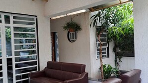 Un área de estar moderna al aire libre con un sofá y sillones de cuero marrón, una mesa de vidrio y vistas a zonas verdes y un edificio al fondo.