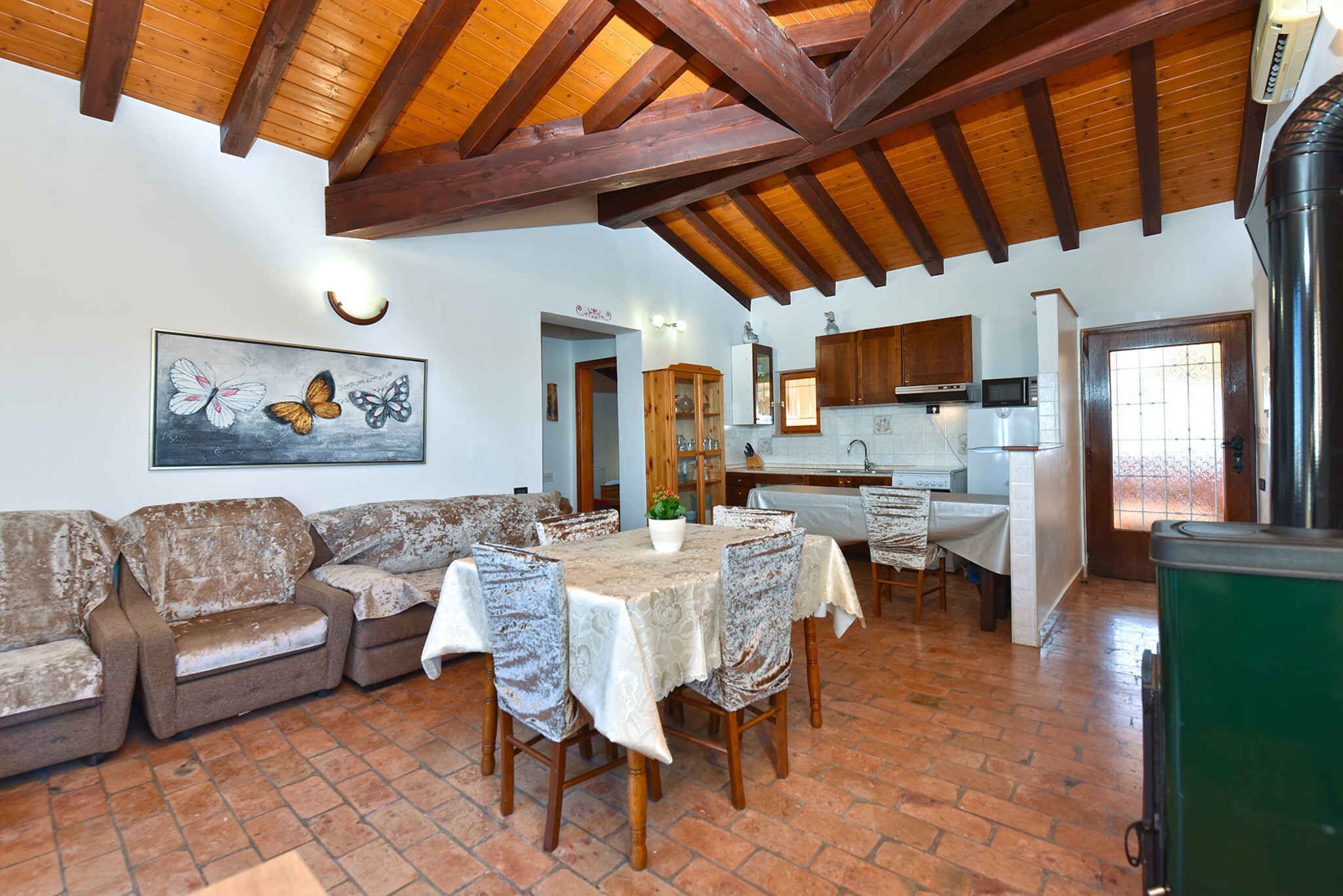 A rustic interior with a wooden ceiling, a dining area with a table and chairs, a kitchen with cabinets and appliances, and a living area with a sofa and a butterfly painting.