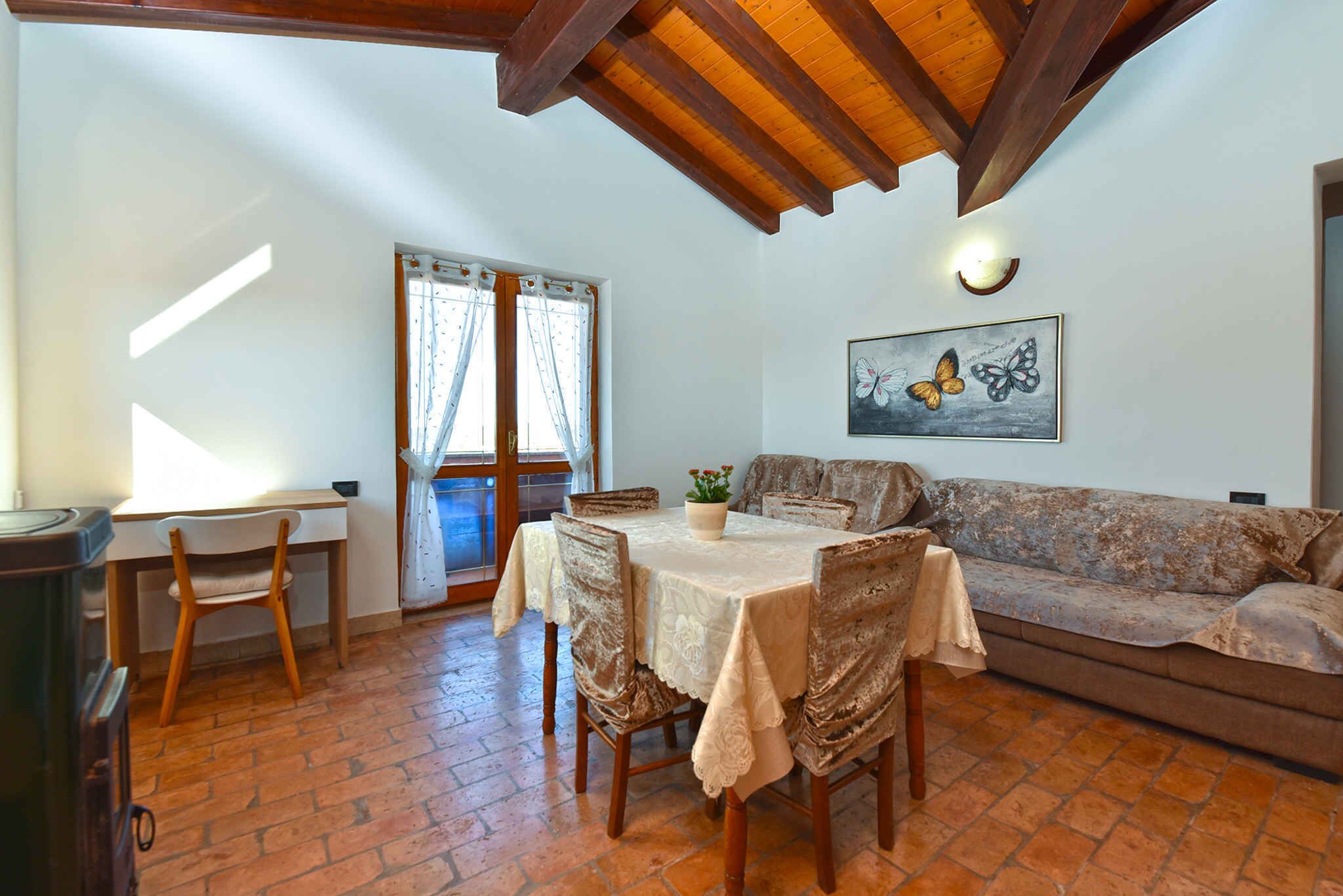 Un comedor con una mesa lista para cuatro personas, un sofá y una ventana con cortinas.