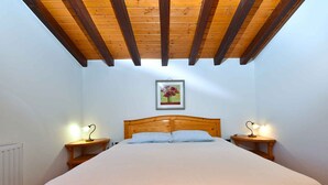 Een slaapkamer met een houten bed, twee nachtkastjes met lampen, een ingelijst foto aan de wand en een schuin houten plafond.