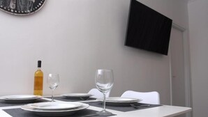 A dining table set with plates, glasses, and a bottle, with a TV mounted on the wall and a door in the background. - Synathens II - Apartments & Studios (Athens)