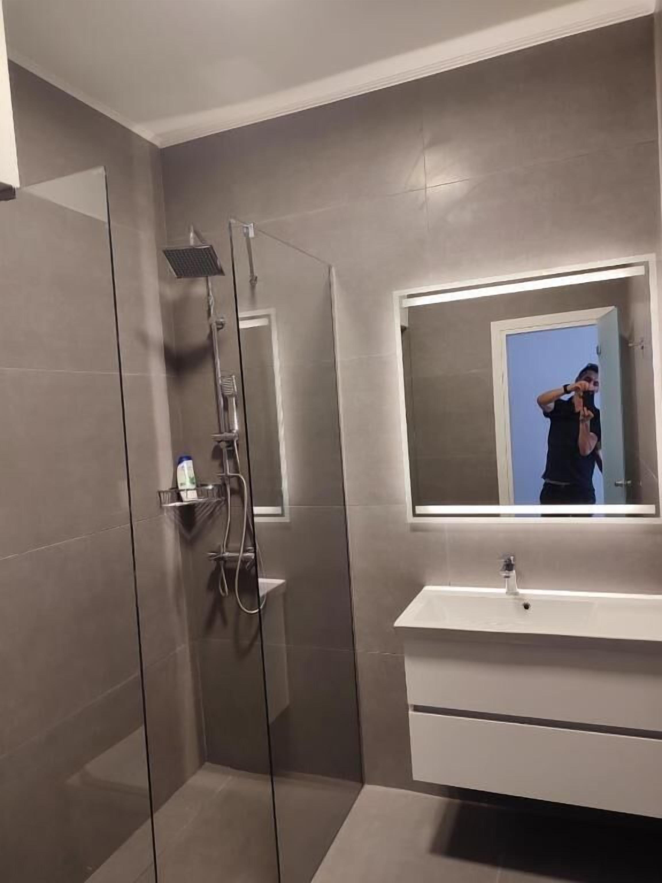 Un bagno moderno con cabina doccia in vetro, uno specchio grande e un mobile lavabo bianco.