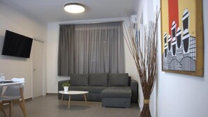 A modern living room with a grey sofa, a small round table, and a TV mounted on the wall. - Synathens II - Apartments & Studios (Athens)