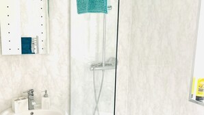 Ein Badezimmer mit weißem Waschbecken, einer Duschkabine aus Glas und einem Spiegel mit Handtuchhalter.