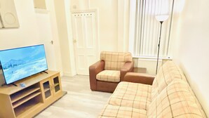 Ein Wohnzimmer mit Fernseher auf einem Holzschrank, einem braunen Sofa und einem Sessel mit Karomuster.