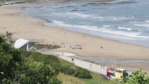 A coastal beach with a paved walkway, a lifeguard tower, and a distant view of a town. - Evergreen Pines (Scarborough)