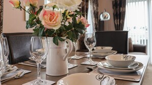 A dining table set with white plates, bowls, and cutlery, a pitcher, and a vase with roses. - Evergreen Pines (Scarborough)