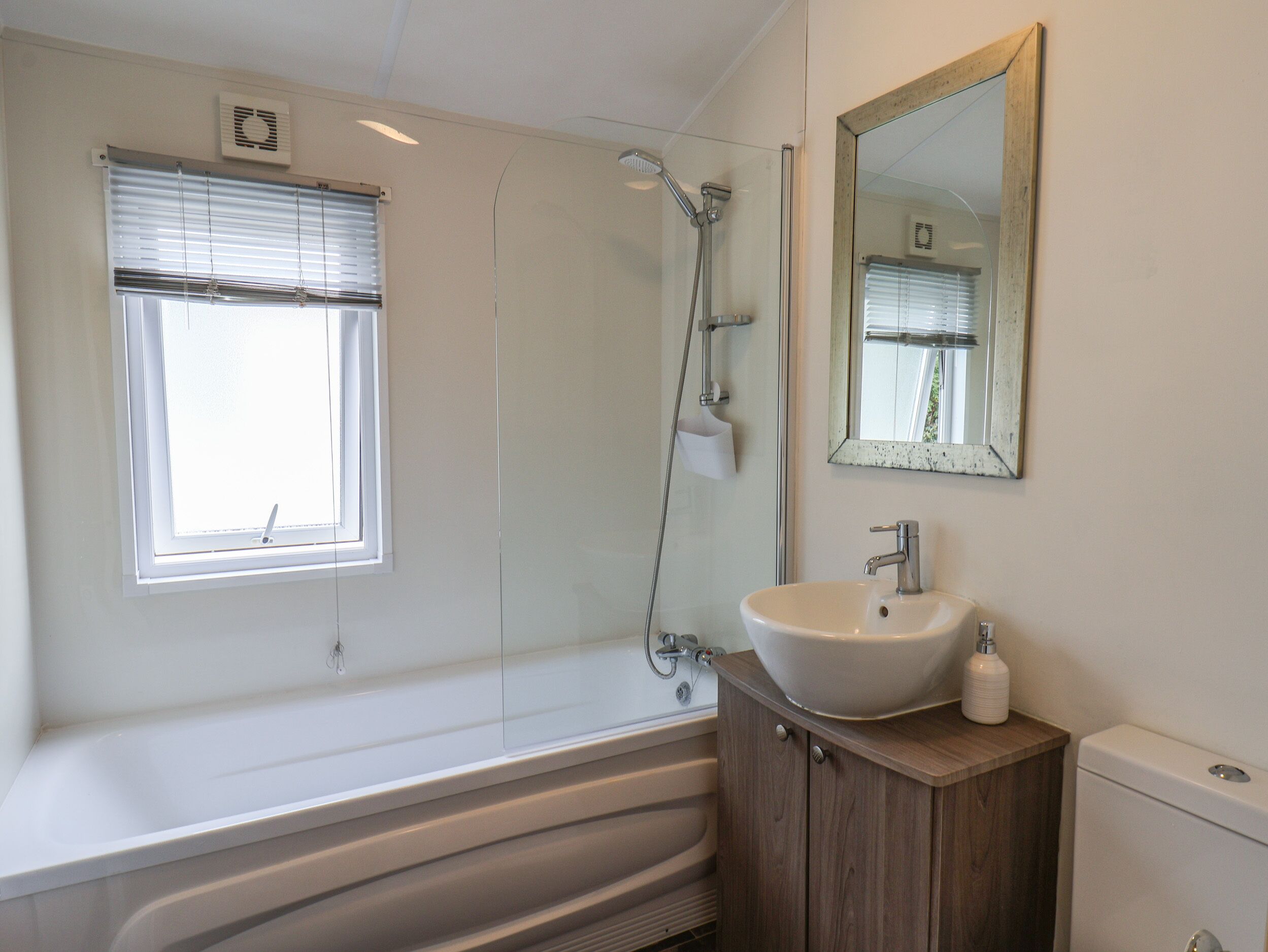 A modern bathroom with a freestanding bathtub, a vanity with a sink, a mirror, and a window with blinds.