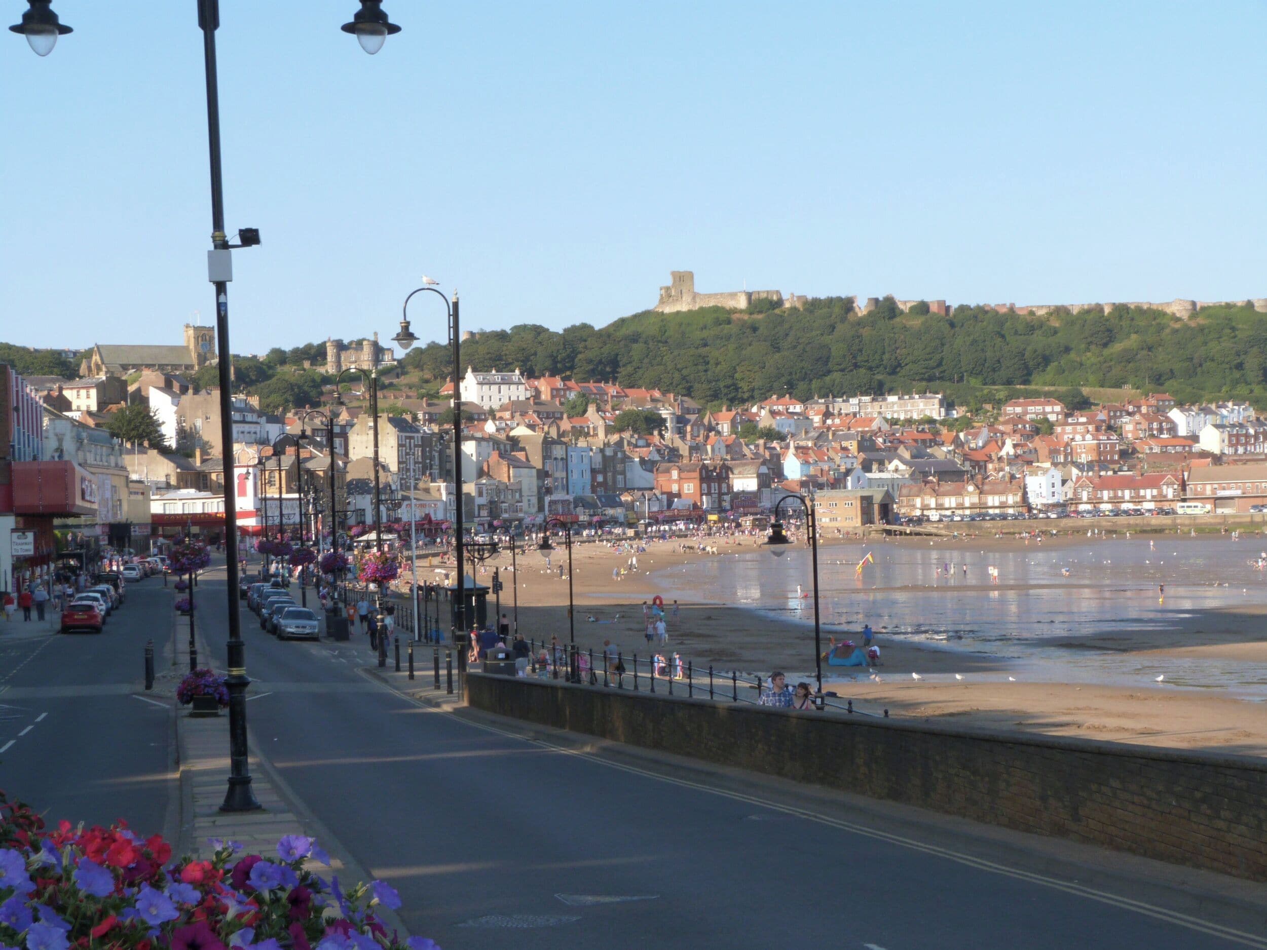 A coastal town with a beach, historic buildings, and a prominent castle on a hill.