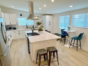Cocina moderna con armarios blancos, una isla central, taburetes de bar y un comedor con mesa y sillas.