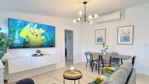 A modern living room with a flat-screen TV, a dining area, and a sofa. - No Tax! Modern 4BR Pool Villa, Hot Tub, Arcade (Anaheim)