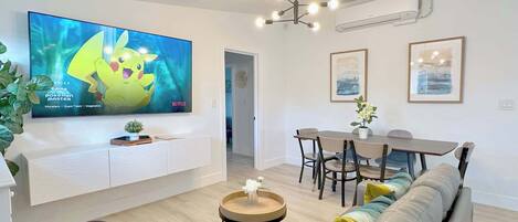 A modern living room with a flat-screen TV, a dining area, and a sofa.