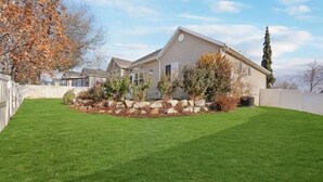 A residential property with a well-maintained lawn, a stone retaining wall, and a house with a gabled roof.