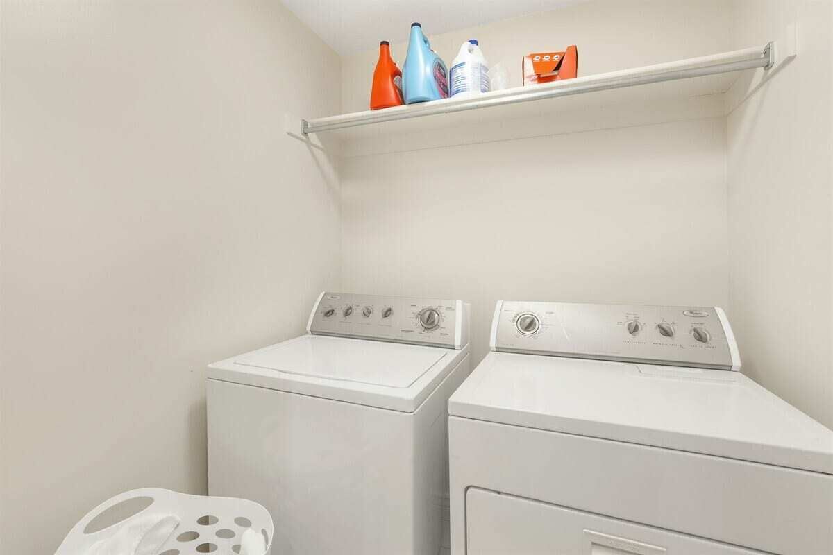 A laundry area with two white washing machines, a shelf with cleaning supplies, and a white laundry basket.