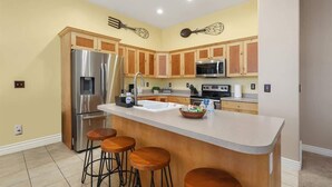 A kitchen with wooden cabinets, stainless steel appliances, a central island with stools, and decorative wall art.