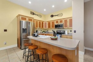 A kitchen with wooden cabinets, stainless steel appliances, a central island with stools, and decorative wall art.