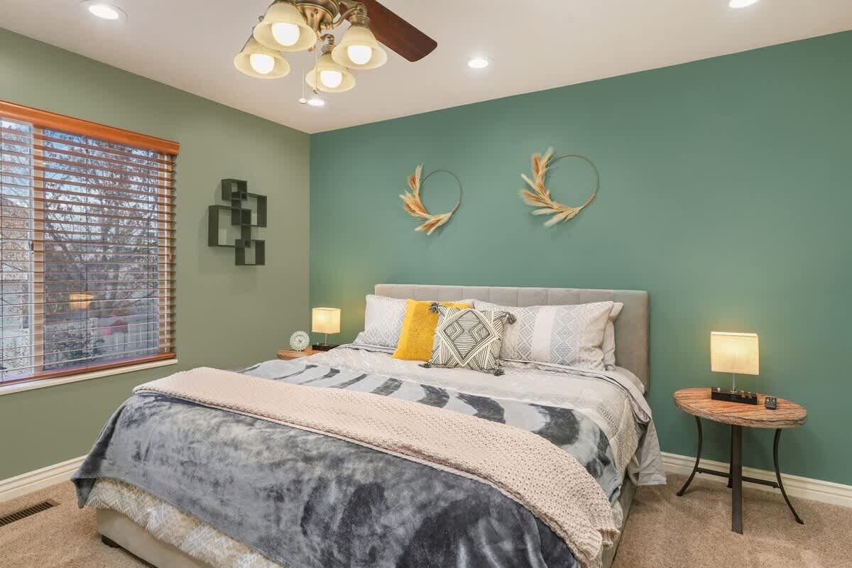 Un dormitorio con una cama, dos mesitas de noche, un ventilador de techo y decoración en la pared.