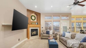 A living room with a fireplace, sofas, a TV, and a ceiling fan.