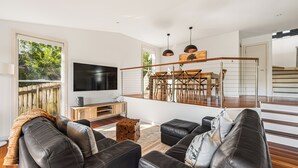 Ein modernes Wohnzimmer mit einem schwarzen Ledersofa, einem Flachbildfernseher und einem Essbereich aus Holz mit einer Treppe.